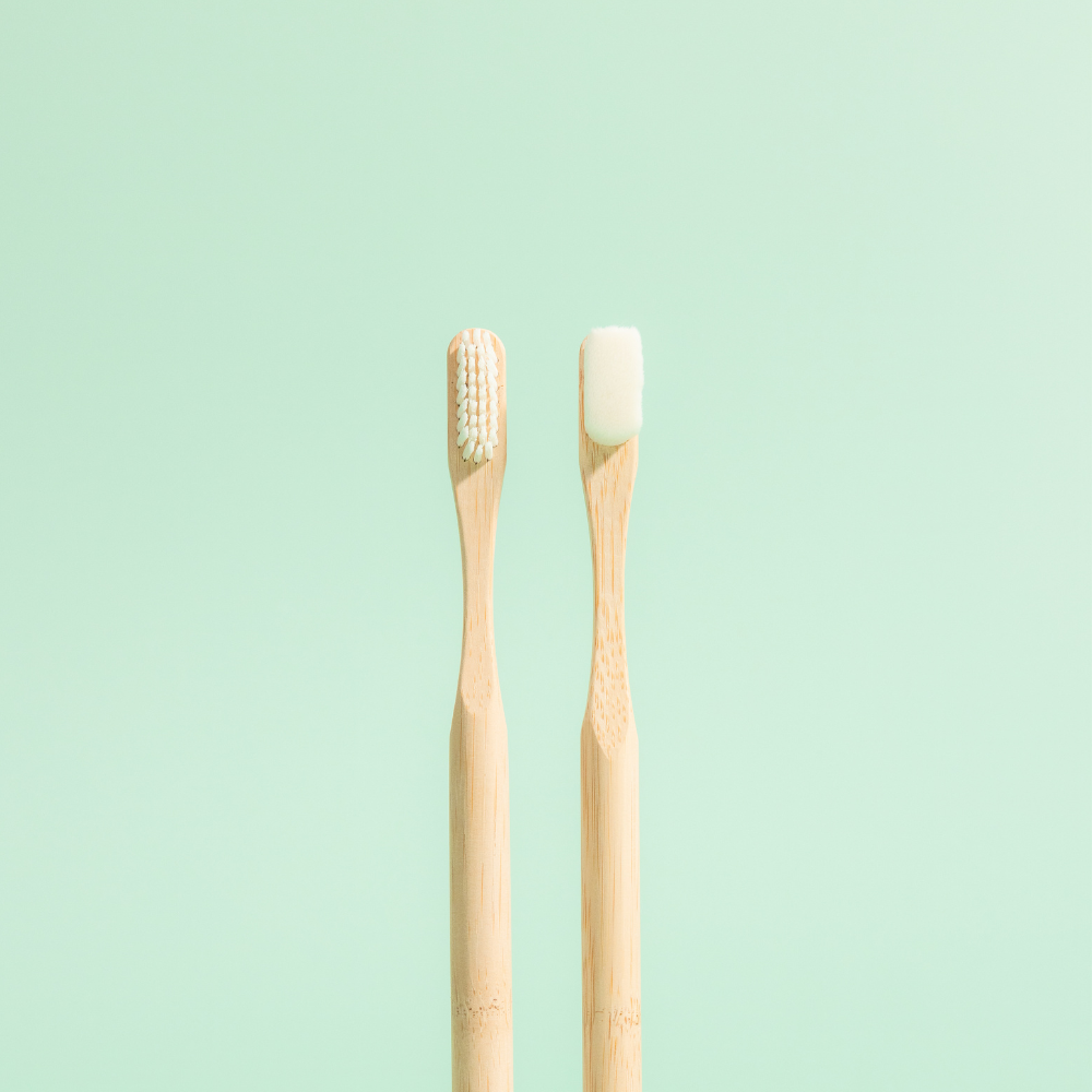Two bamboo toothbrushes with white bristles positioned upright on a light green background.
