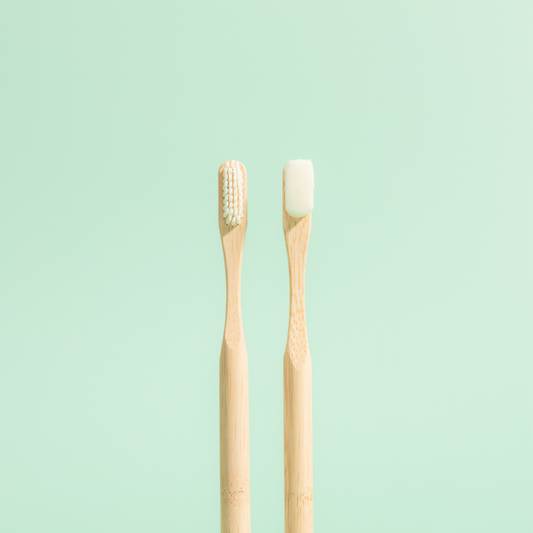 Two bamboo toothbrushes with white bristles positioned upright on a light green background.